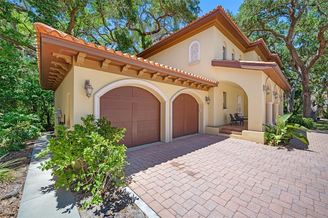 1966 Freedom Dr, Clearwater, FL 33755 - mediterranean / spanish house featuring stucco siding, an attached garage, decorative driveway, and a tiled roof