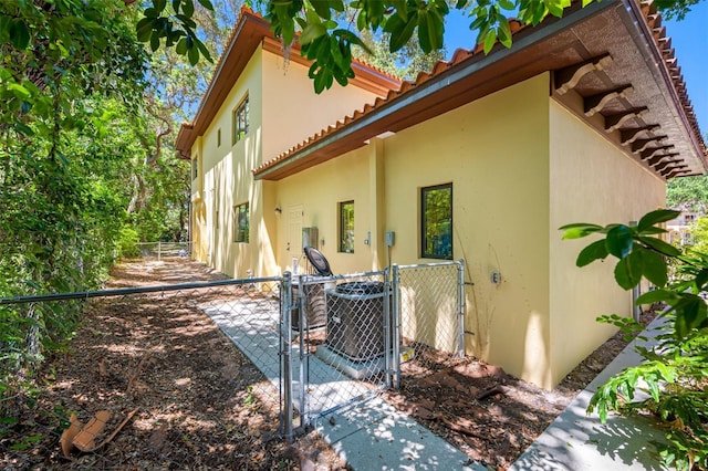 1966 Freedom Dr, Clearwater, FL 33755 - rear view of house featuring a gate, stucco siding, a tiled roof, fence, and central AC unit