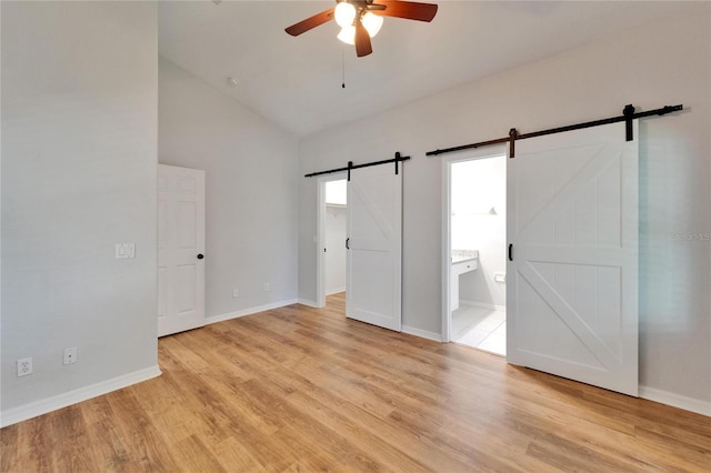 11932 Whisper Creek Dr, Riverview, FL 33569 - unfurnished bedroom featuring a barn door, light wood-style floors, ensuite bathroom, baseboards, and high vaulted ceiling