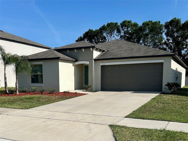 prairie-style home with stucco siding, roof with shingles, a front lawn, concrete driveway, and an attached garage