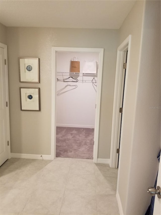 hall featuring baseboards, light tile patterned floors, and light colored carpet