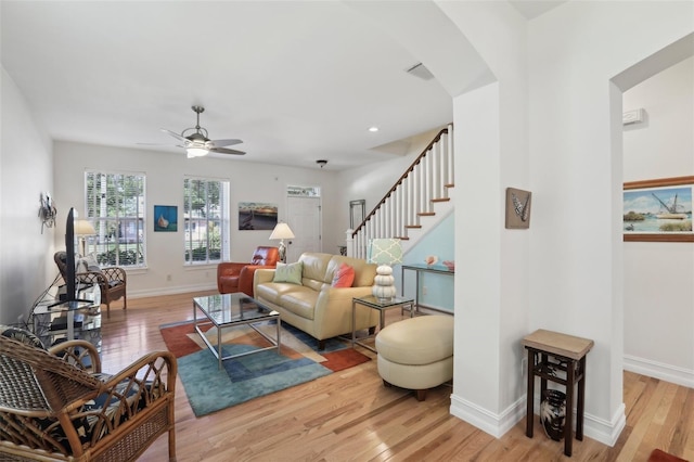 living room with arched walkways, light wood-style floors, ceiling fan, baseboards, and stairway