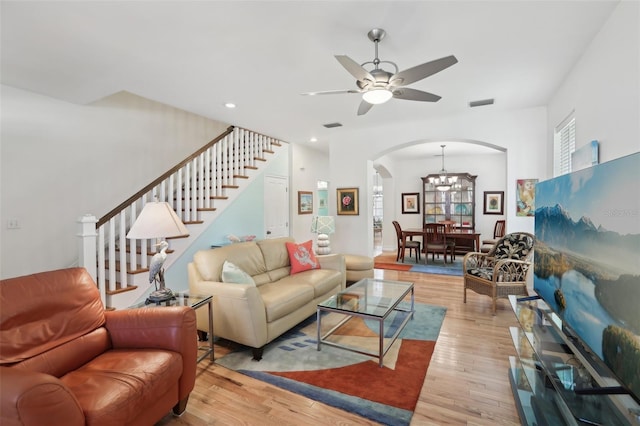 living room featuring arched walkways, stairs, ceiling fan with notable chandelier, light wood finished floors, and visible vents