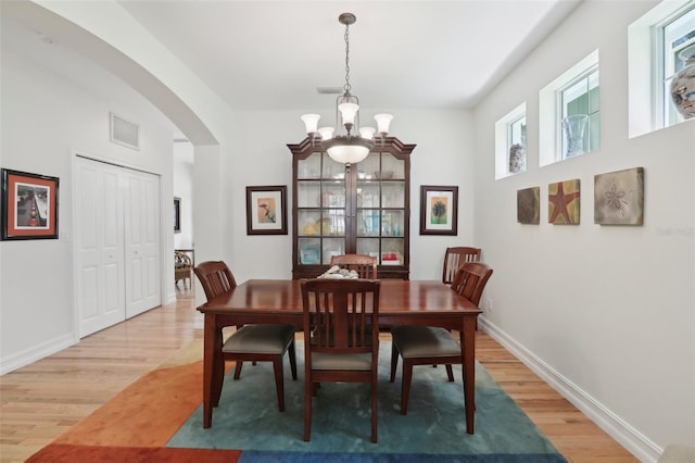 dining space featuring a chandelier, light wood-type flooring, visible vents, baseboards, and arched walkways