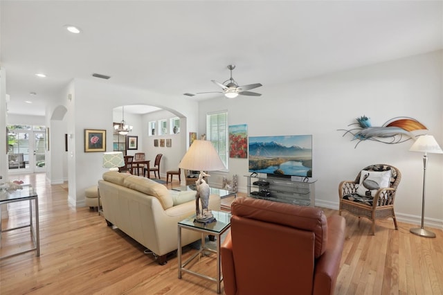 living room with light wood finished floors, visible vents, ceiling fan with notable chandelier, and arched walkways