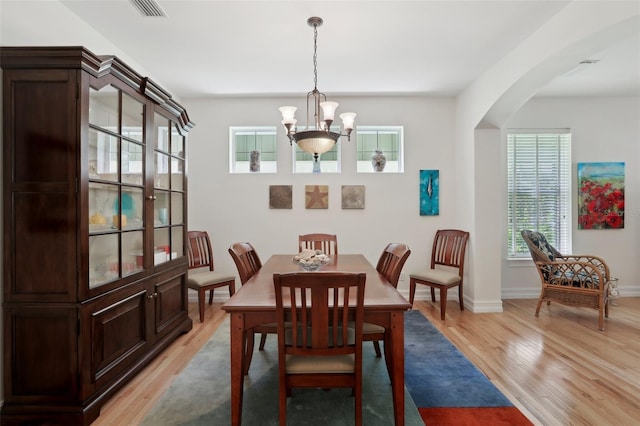 dining area featuring visible vents, baseboards, arched walkways, light wood finished floors, and a notable chandelier