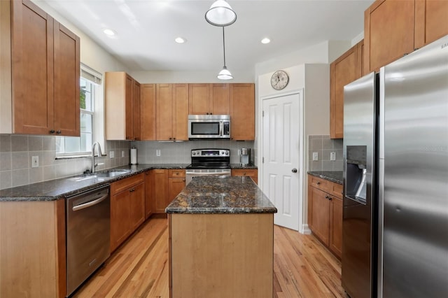 kitchen featuring dark stone countertops, light wood-style flooring, a sink, stainless steel appliances, and a kitchen island
