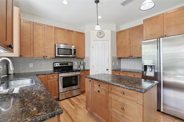 kitchen with appliances with stainless steel finishes, light wood-style floors, a kitchen island, and a sink