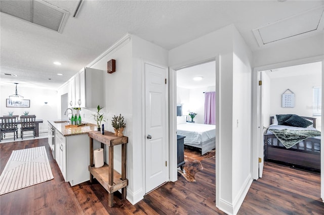 hallway with a sink, visible vents, baseboards, a textured ceiling, and dark wood finished floors