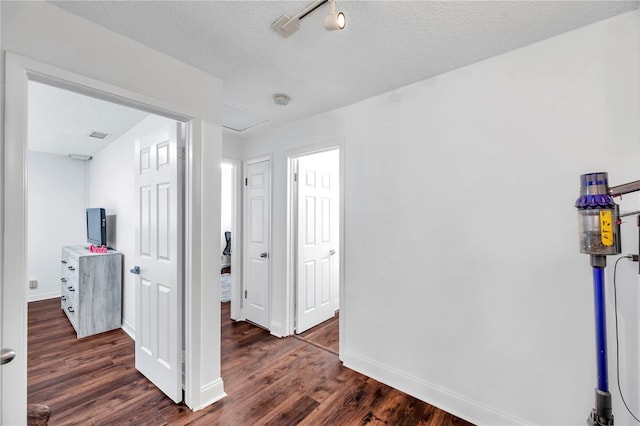 hallway featuring a textured ceiling, dark wood-style flooring, and baseboards