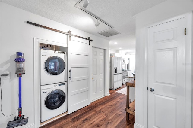 laundry room featuring track lighting, laundry area, a barn door, stacked washer / dryer, and dark wood-type flooring