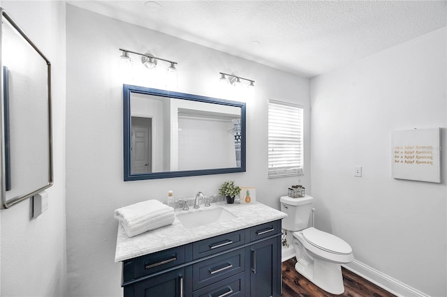 bathroom with wood finished floors, toilet, vanity, baseboards, and a textured ceiling
