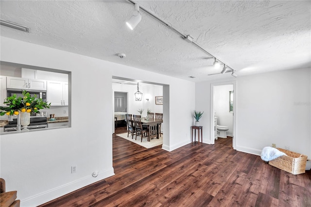 empty room featuring baseboards, dark wood-style flooring, rail lighting, and a textured ceiling