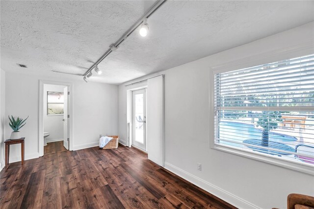 empty room with a textured ceiling, dark wood-style flooring, rail lighting, and baseboards