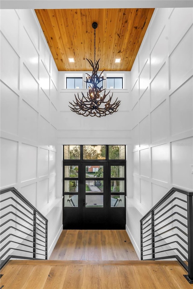 entryway with an inviting chandelier, a decorative wall, a healthy amount of sunlight, wooden ceiling, and hardwood / wood-style flooring
