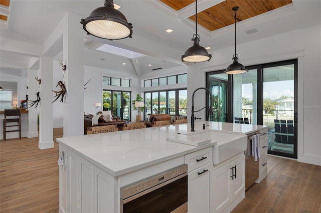 kitchen with light stone countertops, open floor plan, a sink, light wood finished floors, and appliances with stainless steel finishes