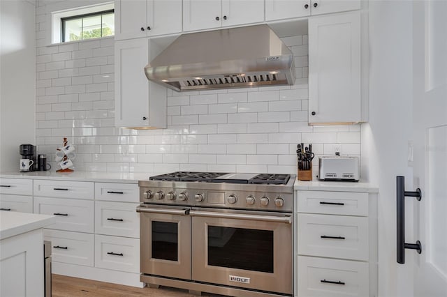 kitchen featuring light countertops, white cabinetry, wall chimney exhaust hood, and range with two ovens