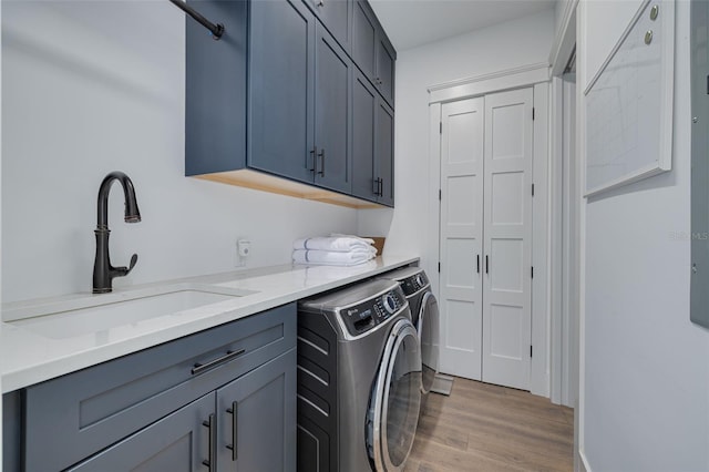 clothes washing area with washer and dryer, a sink, light wood-style flooring, and cabinet space