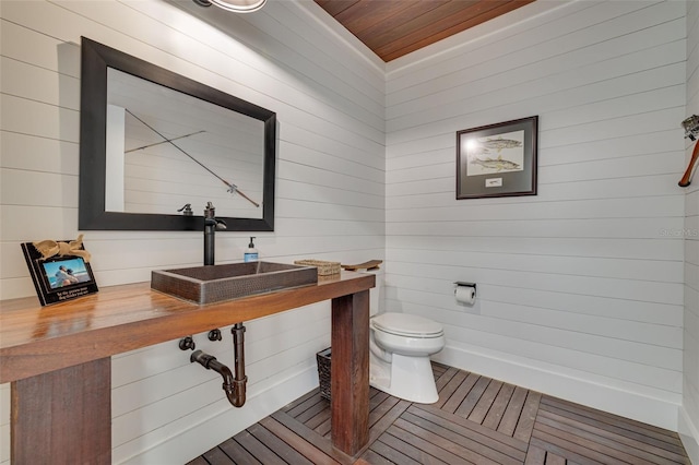 bathroom featuring a sink, wood ceiling, toilet, and wooden walls