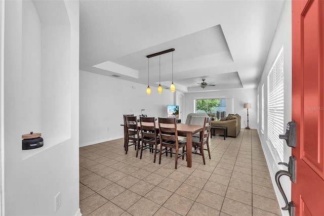 dining space featuring baseboards, light tile patterned floors, a tray ceiling, and ceiling fan