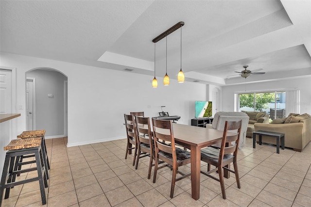 dining area with ceiling fan, arched walkways, light tile patterned floors, a tray ceiling, and visible vents