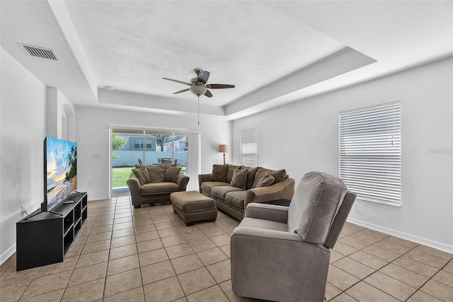 living room featuring ceiling fan, visible vents, light tile patterned floors, and a raised ceiling