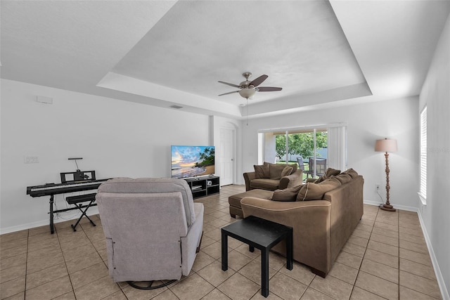 living room with visible vents, light tile patterned flooring, baseboards, a tray ceiling, and a ceiling fan