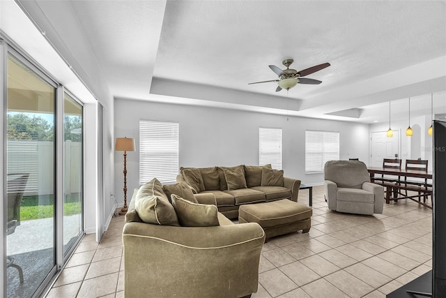 living room featuring a ceiling fan, plenty of natural light, light tile patterned floors, and a raised ceiling
