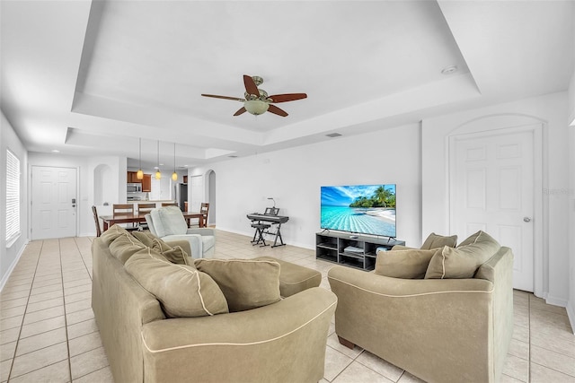 living room with arched walkways, a raised ceiling, ceiling fan, and light tile patterned flooring