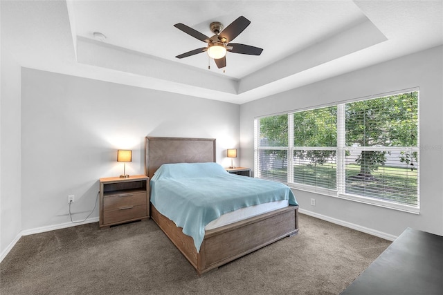 carpeted bedroom with a tray ceiling, ceiling fan, and baseboards