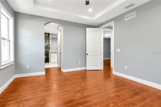 unfurnished bedroom with arched walkways, a raised ceiling, and visible vents