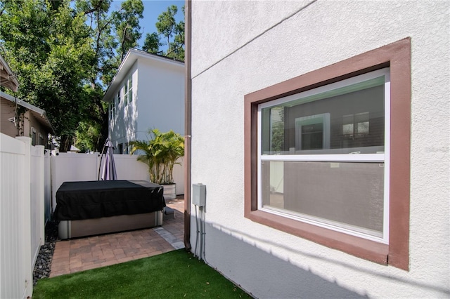 view of side of home featuring a hot tub, fence, a patio area, and stucco siding