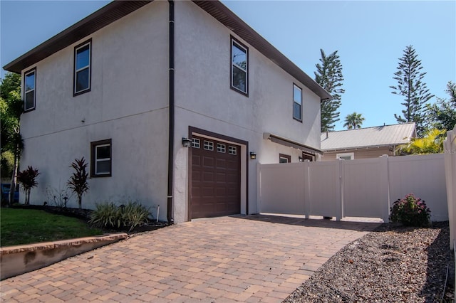 view of side of property featuring fence, decorative driveway, stucco siding, a gate, and an attached garage