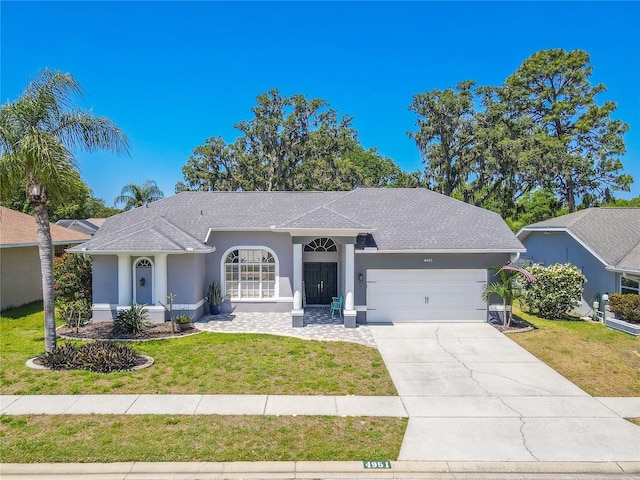 ranch-style home with a garage, a front lawn, roof with shingles, stucco siding, and concrete driveway