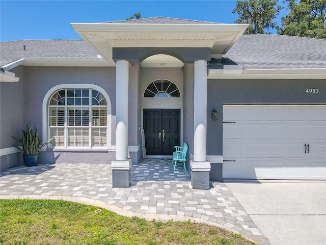 entrance to property with a shingled roof, an attached garage, and stucco siding