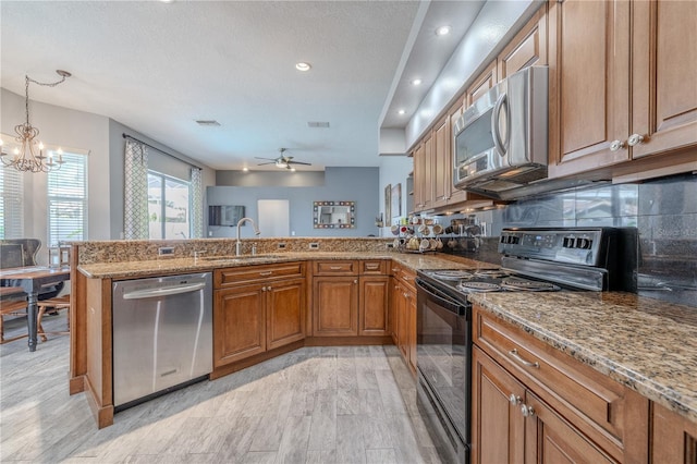 kitchen featuring brown cabinets, light stone countertops, a sink, stainless steel appliances, and a peninsula