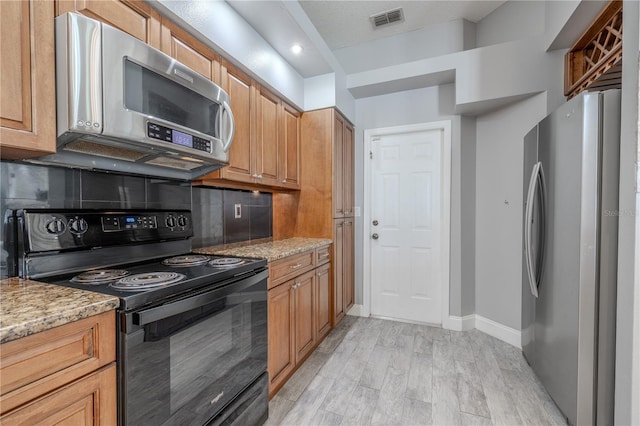 kitchen featuring appliances with stainless steel finishes, light stone counters, light wood-type flooring, backsplash, and visible vents