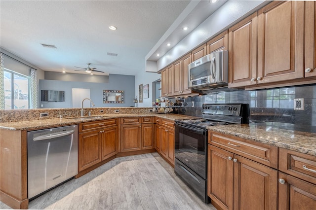 kitchen with brown cabinets, light stone counters, a sink, stainless steel appliances, and a peninsula