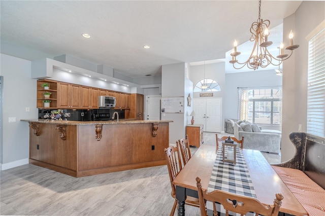 kitchen with brown cabinets, open shelves, light wood-style floors, a chandelier, and stainless steel microwave