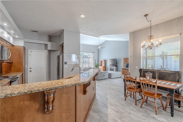 kitchen with visible vents, a textured ceiling, brown cabinets, a sink, and appliances with stainless steel finishes