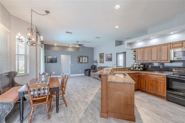 kitchen with light stone counters, a sink, a peninsula, stainless steel microwave, and black / electric stove