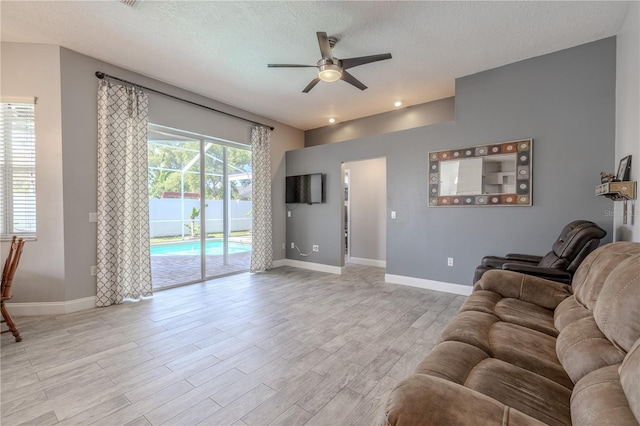 living area with baseboards, a ceiling fan, light wood-style floors, and a textured ceiling
