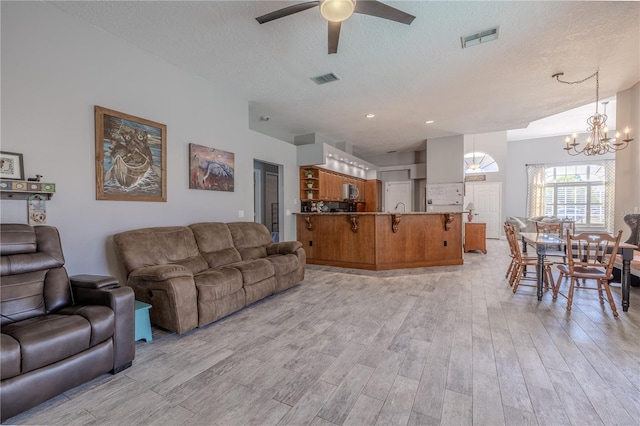 living room with visible vents, a textured ceiling, light wood finished floors, and ceiling fan with notable chandelier