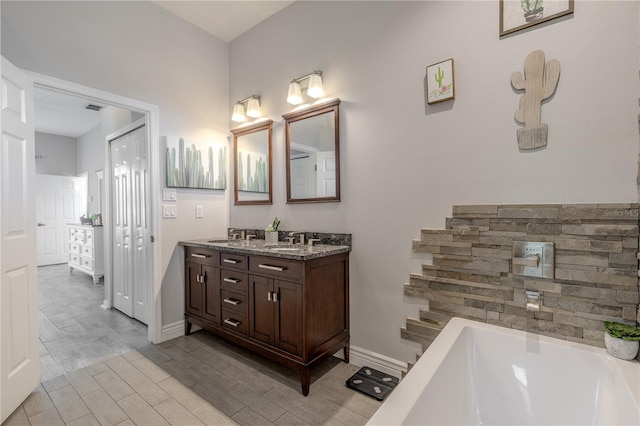 full bath featuring a tub, double vanity, visible vents, wood finished floors, and a sink