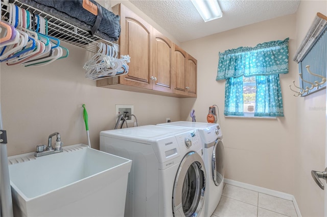 laundry area featuring washing machine and dryer, cabinet space, a sink, light tile patterned floors, and baseboards