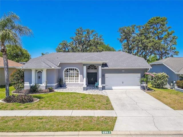 ranch-style house featuring a garage, a front yard, stucco siding, a shingled roof, and concrete driveway