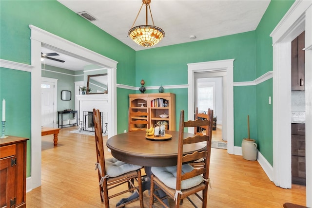 dining room with visible vents, a fireplace with flush hearth, baseboards, ceiling fan with notable chandelier, and light wood finished floors