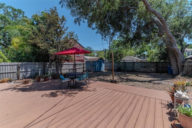 wooden deck featuring a fenced backyard, a storage unit, an outdoor structure, and outdoor dining space