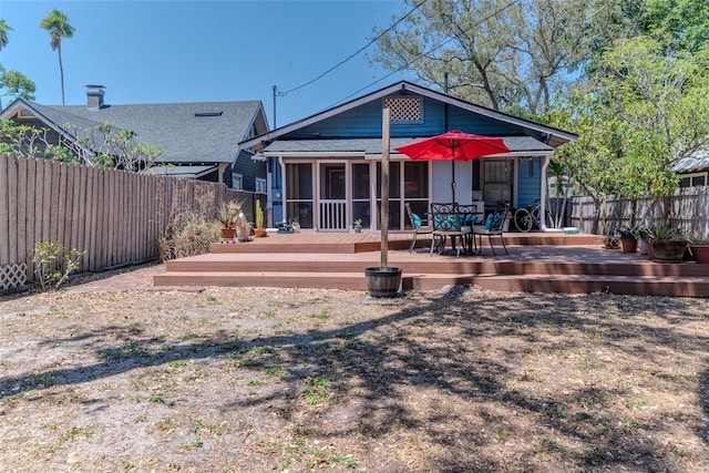 rear view of property featuring roof with shingles, a wooden deck, a fenced backyard, and a sunroom