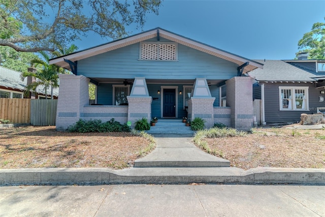 view of front facade with covered porch, brick siding, and fence